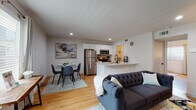 This thoughtfully designed single-floor residence offers a seamless open-concept layout that integrates the living, dining, and kitchen areas into one cohesive and functional space. Warm hardwood flooring runs throughout, unifying each area with a consistent, inviting aesthetic.

The kitchen is outfitted with white shaker cabinetry, stainless steel appliances including a full-size refrigerator, microwave, and range, and a peninsula featuring a quartz countertop with an integrated sink. The peninsula doubles as a casual breakfast bar and naturally separates the kitchen from the dining area, which comfortably accommodates a glass-top dining table and chairs.

The living room is generously proportioned, featuring recessed lighting, a tufted sofa, armchair, glass coffee table, and a media console. Natural light enters through windows dressed with modern blinds and curtains, creating a bright and comfortable atmosphere. A dedicated desk nook near the window provides a practical workspace.

The bedroom is a serene retreat, featuring a ceiling fan, large windows with blinds, and ample room for a king-size bed, nightstands, and a bench at the foot. The bathroom showcases marble-style tile flooring, a white vanity, and a tub-shower combination, maintaining the clean, modern character found throughout the residence.