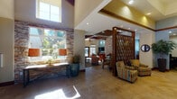 Located in Maple Valley, Washington, this single-story community clubhouse at 22435 SE 240th St offers a thoughtfully designed gathering space with a blend of warm, contemporary finishes throughout. The welcoming lobby greets visitors with large-format tile flooring, soaring ceilings, and an elegant front desk crafted from rich wood tones. A distinctive diamond-patterned wood screen partition divides the entry from adjoining lounge areas, adding architectural interest and visual depth.

The main lounge features dramatic exposed wood beam ceilings, floor-to-ceiling stacked stone accent walls, and abundant natural light streaming through tall windows. Comfortable seating arrangements invite relaxation, complemented by warm neutral tones and curated décor. A secondary lounge area with a wall-mounted flat-screen TV and built-in wood shelving opens directly to the outdoor pool area via glass doors, seamlessly connecting indoor and outdoor living.

The well-appointed kitchen includes rich wood cabinetry, granite countertops, stainless steel appliances, a tile backsplash, and a central island with bar seating — ideal for community gatherings and events. A dedicated prep kitchen with additional cabinetry, granite surfaces, and a garden window overlooking lush greenery provides supplementary functionality. Together, these spaces create a cohesive, inviting environment suited for a variety of community activities.