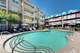 Located in the heart of Atlanta's Grant Park neighborhood, this outdoor amenity space centers around a generously sized, freeform swimming pool with clear turquoise water. The pool's curvilinear design creates an inviting, resort-style atmosphere, complemented by a surrounding pool deck furnished with modern lounge chairs, striped umbrellas, and casual seating areas ideal for relaxing under the open Georgia sky.

The courtyard is enclosed on multiple sides by a multi-story residential building, featuring private balconies that overlook the pool area, providing both privacy and a sense of community. Manicured landscaping with lush shrubs and ornamental trees lines the perimeter, adding greenery and a polished finish to the outdoor environment.

A defining visual feature of the space is a large-scale, colorful mural adorning the adjacent parking structure. The artwork boldly depicts Atlanta's iconic skyline and landmarks in a vibrant, graphic style, serving as a striking urban backdrop that celebrates the city's identity and character. String lights are strung across portions of the courtyard, enhancing the ambiance during evening hours. Grilling stations and additional seating areas round out the amenities, making this courtyard a well-appointed outdoor gathering space in the heart of Atlanta.