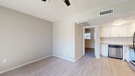 This single-floor unit offers a clean, modern aesthetic with light wood-style flooring running throughout all living areas, bedrooms, and the kitchen, creating a cohesive and contemporary feel. The open layout connects the living area to the kitchen seamlessly, as seen in the overhead floor plan view, providing an efficient and functional use of space.

The living area is bright and airy, featuring a ceiling fan with integrated lighting, a textured ceiling, and a large window that allows natural light to pour in and offers a view to the outdoors. Neutral warm-gray walls throughout contribute to the welcoming ambiance.

The kitchen is well-equipped with crisp white shaker-style cabinetry, granite-look countertops, a classic white subway tile backsplash, and stainless steel appliances including a range, dishwasher, and refrigerator. The design is both stylish and practical.

Bedrooms continue the light flooring and neutral palette, each outfitted with ceiling fans and windows for natural ventilation and light. The bathroom features a granite-top vanity with white cabinetry, wood-style flooring, a full tub-shower combination, and a grab bar for added accessibility. Overall, the space is thoughtfully updated with modern finishes throughout.
