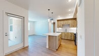 Located at 1151 Encanto Loop in Chula Vista, California, this thoughtfully designed single-floor residence offers a clean, modern aesthetic throughout its well-utilized layout. Light-toned hardwood-style flooring runs consistently across all rooms, contributing to a cohesive and airy feel.

The open-concept kitchen and living area serves as the heart of the home. The kitchen is outfitted with warm, natural wood cabinetry accented by matte black hardware, crisp white quartz countertops, and a geometric herringbone tile backsplash. A central island provides additional prep space and casual seating. Stainless steel appliances, including a refrigerator with ice maker, range, over-the-range microwave, and dishwasher, complete the space. Pendant lighting hangs above the island, complementing the recessed lighting overhead. The adjoining living area is bright and open, with a window allowing natural light to flow in.

The spacious primary bedroom is generously sized and features multiple windows offering neighborhood views, as well as a ceiling fan for added comfort. A walk-in closet provides ample storage, and a hallway connects the bedroom to the rest of the home. Throughout the residence, white walls and clean architectural lines create a bright, welcoming ambiance suited for modern living.