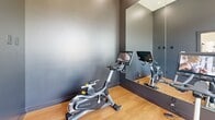 Located at 1480 N 48th St in Springdale, Arkansas, this single-floor fitness center offers a generously sized, thoughtfully designed space for a comprehensive workout experience. The main exercise room is bright and airy, featuring soaring vaulted ceilings, recessed lighting, and large windows that flood the space with natural light and offer views of the surrounding neighborhood. Warm hardwood-style flooring runs throughout, complementing the clean white walls and modern aesthetic.

The exercise room is outfitted with an extensive selection of equipment, including cable machines, multi-function strength stations, free weights, kettlebells, medicine balls, and a dedicated dumbbell rack. Cardio equipment includes treadmills, ellipticals, a rowing machine, and a Matrix stationary bike with an interactive display screen. A dedicated spin/cycling alcove with dark accent walls and floor-to-ceiling mirrors provides a focused environment for cycling workouts.

Full-length mirrors are strategically placed throughout the main floor to enhance the sense of space and support proper form. A large ceiling fan provides airflow across the workout area, while wall-mounted TVs offer entertainment during cardio sessions. A motivational neon "YOU GOT THIS" sign adds an energizing touch. The space also includes a built-in shelving and desk area that serves as the office, providing a functional administrative zone within the facility.