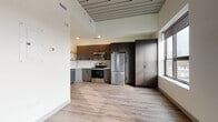 Located at 410 W Broadway St in Mount Pleasant, Michigan, this thoughtfully designed single-floor unit showcases a clean, contemporary aesthetic throughout. The open-concept kitchen is a standout feature, outfitted with dark wood-grain cabinetry that extends floor to ceiling, providing generous storage. Stainless steel appliances — including a French door refrigerator, electric range, over-the-range microwave, and dishwasher — are complemented by light quartz countertops and a white subway tile backsplash. Open shelving adds a modern, functional touch. Light wood-tone luxury vinyl plank flooring flows seamlessly throughout the unit, creating a warm and cohesive aesthetic. A distinctive slatted wood ceiling accent adds architectural character to the kitchen and living area. The living space is bright and open, benefiting from large windows that frame views of the surrounding downtown Mount Pleasant streetscape, allowing ample natural light to fill the room. A ceiling fan adds comfort to the airy bedroom, which also features multiple windows with roller shades. The bathroom is clean and functional, offering a full tub-shower combination, a dark-toned vanity with a white countertop, and wood-look flooring that ties in with the rest of the unit. Overall, this space presents a modern, well-appointed interior with quality finishes in a convenient downtown location.