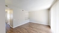 This 2-bedroom, 1-bathroom unit presents a clean, functional single-floor layout designed for efficient everyday living. The combined living and dining area is anchored by durable wood-look flooring that extends throughout the main living spaces, providing a warm and cohesive aesthetic. Built-in shelving along one wall of the living room adds both character and practical storage, while a sliding glass door with vertical blinds allows natural light to filter in. The galley-style kitchen features white cabinetry, light countertops, and black appliances including a refrigerator, range, and dishwasher, all set atop matching wood-look flooring. A pass-through connects the kitchen to the living area, enhancing the open feel of the space. Both bedrooms are carpeted for comfort and equipped with ceiling fans. The primary bedroom offers a generous footprint with a dedicated closet and window with vertical blinds for natural light. The second bedroom is similarly appointed with carpet and its own closet. A hallway connects the bedrooms to the full bathroom, which includes a single-sink vanity with mirror, toilet, and a tiled shower-tub combination, all finished with wood-look flooring for easy maintenance. The neutral color palette throughout creates a bright, move-in-ready environment.