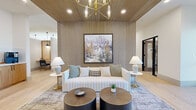 Located at 11575 W Roosevelt St in Avondale, Arizona, this single-story commercial space delivers a refined, modern aesthetic across a generously sized floor plan. The entry makes an immediate impression with a dramatic natural stone accent wall framing black-framed glass doors, setting the tone for the sophisticated interior beyond.

The central lounge area serves as the heart of the space, featuring striking vertical wood slat wall paneling, a slatted wood ceiling, and an elegant brass chandelier that casts warm light throughout. A large-scale landscape painting anchors the lounge's focal wall, complemented by plush seating, layered area rugs, and dark round coffee tables atop light hardwood flooring that flows throughout the entire space.

Multiple hallways connect the various zones, each lined with clean white walls, dark-framed doors, and interior window cutouts offering views into adjoining rooms—including a warmly lit conference or dining area with a woven rattan pendant light. The private office is a serene, well-appointed workspace featuring a built-in wood desk, wood-paneled wall detailing, a large frosted window admitting soft natural light, and a patterned area rug underfoot.

An additional nook with a built-in desk workstation and pendant lighting opens toward glass exit doors, providing views of an outdoor patio area. Throughout the space, the consistent use of warm wood tones, matte black accents, and abundant natural light creates a cohesive, professional, and inviting atmosphere.