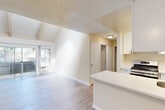 This single-floor, 2-bedroom, 1-bathroom residence offers a well-organized layout with distinct living areas and thoughtful design details throughout. The living room is an immediate standout, featuring soaring vaulted ceilings with exposed wood beams and a textured ceiling finish. Light hardwood-style flooring runs underfoot, and a full-width sliding glass door opens to an outdoor patio, flooding the space with natural light and providing views of surrounding greenery.

The kitchen is positioned adjacent to the living area and features white shaker cabinetry with black hardware, light quartz countertops, a stainless steel double sink, a gas range, and a peninsula that connects the kitchen to the living space. Ample upper and lower cabinet storage maximizes functionality in the efficiently designed layout.

Both bedrooms are carpeted and receive natural light through large windows framing outdoor foliage. The primary bedroom is generously sized, with a ceiling fan and a high clerestory window adding to the airy feel. The shared bathroom includes a white vanity with drawer storage, a light quartz countertop, wood-style flooring, and a grab bar. A dedicated closet provides additional storage. The overall palette of warm neutrals and white finishes creates a clean, cohesive ambiance throughout.