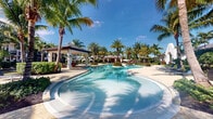 Located at 11020 Town Circle in Royal Palm Beach, Florida, this outdoor community amenity space delivers a resort-caliber experience in a lush, tropical setting. The centerpiece of this area is a beautifully designed freeform swimming pool with crystal-clear turquoise water, its sweeping curves creating an inviting and leisurely atmosphere. The pool is framed by elegant brick pavers that provide a clean, polished surface for lounging and movement throughout the space.

Towering palm trees are planted throughout the grounds, offering natural shade and a distinctly South Florida aesthetic that enhances the resort-like ambiance. Manicured tropical plantings, including vibrant flowering shrubs and neatly trimmed greenery, add layers of color and texture to the landscape. Comfortable lounge chairs are positioned along the pool deck, ideal for relaxing under the abundant Florida sunshine.

A covered pavilion or cabana structure is visible in the background, providing a shaded gathering area for residents. Additional seating areas are thoughtfully distributed across the grounds to accommodate socializing and relaxation. The overall design balances open, sun-drenched spaces with pockets of shade and greenery, creating a welcoming outdoor environment. Bathed in natural Florida light beneath clear blue skies, this amenity area embodies the relaxed, vibrant lifestyle characteristic of South Florida living.