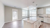 Located at 4600 Bakers Blessing Ln in Summerville, SC, this well-designed single-story home offers three bedrooms and two bathrooms within a thoughtfully laid-out floor plan. The open-concept kitchen and living area serves as the heart of the home, highlighted by a central island with quartz-style countertops, crisp white cabinetry, a white tile backsplash, and stainless steel appliances. Pendant lighting and abundant natural light from multiple windows create a bright, welcoming atmosphere. Wood-look plank flooring flows throughout the main living areas, complemented by neutral warm-gray walls and clean white trim. The living and dining area benefits from a ceiling fan and direct exterior door access. The primary bedroom features plush carpeting, a double-door closet, and a private en suite bathroom with a dual-sink vanity, wood-look flooring, and a separate water closet. The secondary bedrooms also offer carpet flooring and ample natural light through large windows with blinds. The second full bathroom includes a tub-shower combination with white subway tile surround and a single-sink vanity. A dedicated closet provides additional storage. The overall aesthetic is modern, clean, and move-in ready.