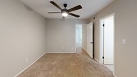 Located at 5200 N Lamar Blvd in Austin, TX, this one-bedroom, two-bathroom unit offers a well-organized single-floor layout that makes efficient use of its compact footprint. The galley-style kitchen is notably updated, featuring white shaker cabinets with matte black hardware, white quartz countertops, a stainless steel sink, wood-look luxury vinyl plank flooring, and black appliances including a refrigerator and dishwasher. A skylight-style ceiling fixture provides overhead illumination, keeping the space bright and functional.

The living area and bedroom are carpeted in a neutral tan tone and finished with soft gray walls, contributing to a calm, cohesive aesthetic throughout. The bedroom accommodates a comfortable furniture arrangement and includes a ceiling fan with light, as well as a window with blinds that admits natural light. Ceiling fans are present in multiple rooms, enhancing airflow and comfort.

The bathroom features a full tub-shower combination with white square tile surround and matte black fixtures, maintaining the consistent design language found throughout the unit. A dedicated in-unit laundry area houses a stacked washer and dryer alongside open shelving, adding practical storage and convenience. The unit's layout and finishes make it a well-appointed option in central Austin.