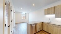 Located at 1 Atlantic St in downtown Stamford, Connecticut, this single-floor unit offers a thoughtfully designed open-concept layout with modern finishes throughout. The kitchen is a standout feature, equipped with warm-toned wood cabinetry, a full suite of stainless steel appliances including a refrigerator, electric range, microwave, and dishwasher, complemented by clean white subway tile backsplash and light quartz-style countertops. A peninsula with additional cabinetry and counter space connects the kitchen seamlessly to the living area, making the layout ideal for both everyday living and entertaining. The living space is bright and airy, benefiting from a large, black-framed grid window that frames views of the surrounding Stamford cityscape and invites generous natural light into the room. Recessed lighting throughout ensures well-lit interiors at any hour. Wood-look flooring runs consistently across the main living areas, lending warmth and a cohesive aesthetic. The bathroom is finished with marble-look tile flooring, a wood-vanity with a quartz countertop, a framed mirror, and a tub-shower combination with white tile surround. The overall design palette—neutral walls, natural wood tones, and stainless accents—creates a clean, contemporary ambiance suited to urban living in the heart of Stamford.