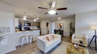 This single-story, one-bedroom, one-bathroom residence offers a thoughtfully arranged layout that maximizes its compact footprint. The open-concept main living area seamlessly integrates the kitchen, dining, and living spaces under a ceiling fan with integrated lighting, creating an airy, connected atmosphere. Light-toned wood-style flooring runs throughout the main areas, contributing to a cohesive and clean aesthetic.

The kitchen is a functional highlight, featuring a peninsula island with bar seating, pendant lighting, medium-toned cabinetry with contemporary hardware, white countertops, and black appliances including a range, microwave, and refrigerator. A dedicated dining area adjacent to the kitchen comfortably accommodates a four-seat table.

The living room benefits from multiple windows fitted with horizontal blinds, allowing natural light to brighten the neutral-toned walls. The bedroom offers a comfortable, well-proportioned space with a ceiling fan, large window, and carpeted flooring. The bathroom includes a full tub-shower combination. A closet provides additional storage. Overall, the space presents a clean, modern, and efficiently designed layout suitable for single occupancy or couples.