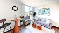 Located at 1221 Ala Kapuna St in Honolulu, Hawaii, this thoughtfully designed unit offers a clean, modern aesthetic throughout its single-floor layout. The open-concept living area is anchored by large floor-to-ceiling windows that flood the space with natural light and frame views of the surrounding Honolulu cityscape. Dark hardwood-style flooring runs throughout, providing a warm contrast to the bright white walls and trim. A dedicated dining nook with a bistro-style table sits adjacent to the living area, making the most of the well-proportioned layout. The kitchen features white shaker cabinetry with brushed nickel hardware, light countertops, a double sink, and full appliances including a range, microwave, and refrigerator. In-unit laundry is also accessible off the main living space. The bedroom is a serene retreat with its own large sliding glass windows offering outdoor views, a ceiling fan, and a walk-in closet. The bathroom is finished with white cabinetry, a single vanity with a wide mirror, and light countertops, maintaining the clean and cohesive palette found throughout the unit. With ample natural light, modern finishes, and a functional open floor plan, this Honolulu residence offers a comfortable island living experience.