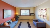 This single-floor unit offers a practical and comfortable layout with well-defined living spaces throughout. The kitchen is efficiently designed in an L-shaped configuration, featuring white cabinetry with wood-trimmed accents, white appliances including a refrigerator, electric range, dishwasher, and built-in microwave, along with a double-basin sink and ample counter space. A large skylight-style overhead fixture brightens the kitchen, and a dedicated closet just off the kitchen houses a stacked washer and dryer for in-unit laundry convenience. The living room features a striking terracotta-orange accent wall that adds warmth and character to the space. A large window with blinds allows natural light to fill the room, which is equipped with a window air conditioning unit and baseboard heating. The bedrooms are bright and well-proportioned, each featuring light wood-style laminate flooring, wood-trimmed windows with blinds that let in natural views of the surrounding greenery, textured ceilings, and baseboard heating. The consistent use of light-toned walls and warm flooring throughout creates a cohesive and inviting atmosphere across all rooms.