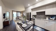Located at 10920 Garfield Ave in South Gate, California, this single-floor residence showcases a thoughtfully designed contemporary interior with a cohesive neutral color palette and upscale finishes throughout. The open-concept living, dining, and kitchen area forms the heart of the home, with dark hardwood-style flooring, recessed lighting, and large windows dressed in sheer curtains that invite an abundance of natural light. A private balcony with modern metal railings extends the living space outdoors, providing a comfortable spot for relaxation. The kitchen is well-appointed with sleek white flat-panel cabinetry, stainless steel appliances including a refrigerator, gas range, microwave, and dishwasher, complemented by a textured hexagonal tile backsplash and ample counter space. The bedroom is a serene retreat, highlighted by a striking diagonal wood slat accent wall, a large window with soft draping curtains, and generous closet storage. The bathroom features a full tub-shower combination, dark wood-style flooring, and clean white finishes. Warm wood accent panels recur throughout the living and sleeping areas, lending the space a refined, design-forward character that ties the entire residence together.