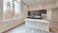 Located at 70 Church Street in Flemington, NJ, this thoughtfully designed 2-bedroom, 1-bathroom residence offers a clean, modern aesthetic across a well-appointed single floor. Light-toned luxury vinyl plank flooring flows seamlessly throughout, complementing the neutral palette of soft whites and warm greiges that define the interior.

The open-concept kitchen and living area serves as the heart of the home, anchored by a striking white kitchen island with an undermount sink. Dark espresso cabinetry lines the kitchen walls, paired with stainless steel appliances and sleek pendant lighting overhead. Tall windows flood the space with abundant natural light and provide views of the surrounding streetscape.

The generous primary bedroom features a spacious double-door closet with black hardware accents and soaring ceilings, creating an airy, comfortable retreat. The second bedroom also benefits from large windows with outdoor views and light-filled interiors. Three closets total provide ample storage throughout the unit.

The bathroom showcases a white shaker-style vanity with quartz countertop, a black-framed rectangular mirror, and modern matte black fixtures — a refined, contemporary touch. A dedicated laundry area and a well-lit hallway with a recessed access panel complete the functional layout. The dining room features additional cabinetry with gold-tone hardware and natural light from a nearby window.