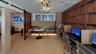 Located at 3001 Crockett St in Fort Worth, Texas, this single-floor amenity space blends contemporary design with warm, eclectic character. The layout is anchored by a welcoming entry area framed by floor-to-ceiling glass doors that invite abundant natural light and offer views of the surrounding streetscape.

A standout bookshelf-mural wall adds a rich, library-inspired aesthetic near the entrance, where a workstation is conveniently positioned for quick tasks. The business center features a dedicated computer workstation area set against the same wood-toned bookshelf backdrop, complemented by a sculptural multi-arm ceiling light fixture that serves as a striking focal point throughout the space.

A built-in banquette seating nook with ambient underlighting, patterned accent pillows, and a round marble-top table provides a comfortable and inviting area to gather or work. Sliding barn doors crafted from mixed wood tones partition the space into distinct zones, adding a rustic-industrial design element that contrasts beautifully with the modern furnishings.

A dedicated media lounge features plush navy leather seating, a wall-mounted flat-screen television, and decorative woven disc wall art, creating a cozy and visually dynamic retreat. Natural stone accent walls and textured wallcoverings throughout contribute depth and warmth, while woven carpet flooring unifies the entire space with a grounded, organic feel.