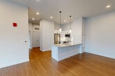 This well-appointed 2-bedroom, 1-bathroom residence in Natick, MA offers a clean, modern aesthetic throughout its single-floor layout. The open-concept living, dining, and kitchen area serves as the heart of the home, anchored by a central island with granite countertops and a built-in sink. The kitchen is fully equipped with white shaker cabinetry featuring matte black hardware, stainless steel appliances including a refrigerator, range, and microwave, and recessed lighting complemented by stylish pendant lights above the island. Warm hardwood-style flooring flows through the main living areas, adding a sense of continuity and warmth. A well-lit hallway connects the main living space to the private quarters, where two bedrooms offer plush carpeting and windows with outdoor views. The primary bedroom is a comfortable size and features a double-door closet, with additional closets providing generous storage throughout the unit. The bathroom is finished with a glass-enclosed walk-in shower with tile surround and mosaic tile flooring, a white vanity with quartz countertop, and modern chrome fixtures. An in-unit laundry area adds convenience to this thoughtfully designed home.