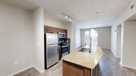 Located in the heart of Austin's vibrant Domain district, this one-bedroom, one-bathroom residence offers a thoughtfully designed layout across a single floor. The open-concept kitchen serves as the centerpiece of the living area, anchored by a sweeping granite-topped island with a built-in sink and elegant pendant lighting overhead. Rich dark cabinetry, a classic tile backsplash, and a full suite of stainless steel appliances — including a refrigerator, range, and microwave — complete the kitchen's polished, functional aesthetic. Track lighting adds a modern touch, while hardwood-style flooring extends throughout the main living area, lending warmth and continuity to the space. The bedroom is a comfortable retreat finished with plush carpeting, a ceiling fan, and a generous window that invites natural light and outdoor views. An adjacent walk-in closet provides ample shelving and hanging storage. The bathroom features a tiled soaking tub and hardwood-style flooring, connecting seamlessly to the bedroom. Neutral tones throughout the residence create a clean, versatile backdrop, making this a practical and inviting home in one of Austin's most sought-after neighborhoods.