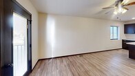Located at 571 225th St in Box Elder, South Dakota, this one-bedroom, one-bathroom unit offers a thoughtfully designed single-floor layout. The open-concept living area seamlessly integrates the living room, dining space, and kitchen, creating an airy and functional environment. Light wood-tone flooring runs throughout the main living areas, complemented by neutral wall tones and dark baseboards that add a clean, contemporary contrast. A ceiling fan with lighting anchors the living room, which also features a glazed entry door leading to a private balcony.

The kitchen is a standout, boasting rich dark cabinetry, light granite-style countertops, a large central island with a double-basin sink and elegant pendant lighting, and a full suite of stainless steel appliances including a range, over-the-range microwave, dishwasher, and refrigerator with ice maker. Recessed lighting adds brightness to the space.

The bedroom is carpeted for comfort, features a ceiling fan, a window for natural light, and includes access to two closets as well as an in-unit laundry area. The bathroom is equipped with a full tub-shower combo. Additional utility and entrance spaces complete this efficiently organized home.