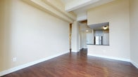 This single-floor unit showcases a thoughtfully designed open-concept layout that seamlessly connects the living area to the kitchen. Rich, dark hardwood flooring extends throughout the main living spaces, complementing the warm neutral-toned walls and crisp white baseboards. The living area is characterized by notably elevated ceilings with exposed structural beams, lending an airy, loft-like quality to the space.

The kitchen is well-appointed with white shaker-style cabinetry, dark granite countertops, a classic subway tile backsplash, and a full suite of stainless steel appliances, including a refrigerator, range, microwave, and dishwasher. A raised breakfast bar separates the kitchen from the main living area, offering a practical and social transition between the two spaces.

The bedroom benefits from abundant natural light streaming through large, black-framed windows that frame striking city skyline views, with exposed brick detailing adding textural character to the room.

The bathroom features light tile flooring, a pedestal sink, a mirrored medicine cabinet with overhead lighting, and a full soaking tub with a shower surround, presenting a clean and functional design.