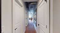 This contemporary urban residence seamlessly blends industrial and modern design across a single thoughtfully planned floor. The open-concept living area is anchored by large windows that flood the space with natural light and frame striking city skyline views. Exposed metallic ductwork runs along the ceilings, adding an industrial-chic character that complements the light-toned walls and warm hardwood flooring found throughout.

The kitchen is well-appointed with crisp white cabinetry, a classic subway tile backsplash, light quartz countertops, and stainless steel appliances including a gas range and built-in microwave. A large window brings in additional natural light, enhancing the bright, clean aesthetic. The adjacent dining area benefits from corner windows on two sides, offering panoramic urban views and an airy atmosphere ideal for entertaining.

The living room is generously proportioned, featuring track lighting, exposed ductwork overhead, and expansive windows overlooking the cityscape. Two bedrooms provide comfortable retreats, each with hardwood floors, large windows with urban views, and ample natural light. The bathroom is finished with elegant marble-style tile on both the floors and shower surround, with a sliding glass shower enclosure adding a sleek, modern touch. A hallway lined with framed artwork and white paneled doors connects the private spaces with understated elegance.
