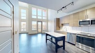 This modern two-story residence at 1911 S Josephine St in Denver's vibrant Washington Park neighborhood offers a thoughtfully designed layout across two floors. The main level impresses immediately with soaring double-height ceilings and a dramatic wall of floor-to-ceiling windows that flood the open-concept living and dining areas with abundant natural light while framing neighborhood views. Dark hardwood flooring runs throughout the main level, lending warmth and contrast to the bright, neutral palette. A private balcony is accessible directly from the living area, extending the space outdoors. The contemporary kitchen is well-appointed with flat-front wood-toned cabinetry, a white tile backsplash, stainless steel appliances including a refrigerator, range, microwave, and dishwasher, and a freestanding island with a white countertop. A dedicated laundry area and multiple closets add practical convenience. Upstairs, the generously sized primary bedroom features plush carpeting, a ceiling fan, and built-in wood cabinetry providing ample storage. The full bathroom on the main level is finished with large-format white tile flooring and a soaking tub with a tiled surround. The open staircase with a sleek metal railing connects both levels, completing this well-designed urban home.