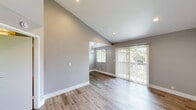 Located at 10990 Del Norte St in Ventura, California, this efficiently designed single-floor unit offers a thoughtfully arranged layout encompassing a living area, dining room, kitchen, bedroom, bathroom, and closet. The living and dining areas are characterized by striking vaulted ceilings that amplify the sense of space, complemented by light gray walls, recessed lighting, and warm wood-look flooring throughout. A sliding glass door floods the living area with natural light and provides views of lush outdoor greenery. The dining space features a decorative pendant light fixture, adding a refined touch. The kitchen is well-equipped with white shaker cabinetry, granite-style countertops, a stainless steel sink, and stainless steel appliances including a refrigerator and range. The bedroom is generously proportioned with mirrored sliding closet doors, large windows overlooking mature trees, and the same consistent wood-look flooring. An adjacent area leads to a bathroom featuring a full tub/shower combination with a curtain rod and a frosted window for natural light. White vanity cabinetry and a well-lit mirror complete the bathroom. The unit presents a clean, modern aesthetic with a cohesive neutral palette throughout.