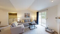 Located in Lynnwood, WA, this one-bedroom, one-bathroom residence offers a thoughtfully designed single-floor layout that maximizes comfort and functionality. The living room is a standout space, featuring soaring vaulted ceilings that create an airy, open atmosphere, soft carpeting, and a tile-surround corner fireplace. A sliding glass door floods the room with natural light and opens to a private balcony with views of surrounding greenery. The kitchen is positioned adjacent to the dining area in an open-concept arrangement, featuring white cabinetry with wood trim accents, a peninsula with countertop seating, track lighting, and wood-look flooring that extends into the dining space. The dining area accommodates a full dining set and includes a ceiling fan. The bedroom offers a carpeted retreat with a large window framing outdoor views, a baseboard heater, and easy access to the closet and hallway. The bathroom presents a wide vanity with a large mirror, a shower-tub combination, and warm wood-look flooring. A dedicated hallway connects all rooms efficiently, completing this well-organized and comfortable Lynnwood residence.