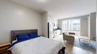 Located at 515 SE Huron Blvd in Minneapolis, MN, this studio unit offers a well-designed open-concept layout that maximizes every square foot. Light hardwood flooring runs throughout the main living area, complementing the neutral gray-and-white color palette that gives the space a clean, modern feel.

The combined living, dining, and kitchen area is anchored by a large window that floods the space with natural light and provides views of the surrounding neighborhood. The kitchen features white cabinetry, a dark countertop, a subway tile backsplash, stainless steel appliances, and track lighting overhead. The living area offers enough room for a sofa, coffee table, and wall-mounted television setup.

A partial dividing wall subtly separates the sleeping area from the rest of the living space, creating a sense of definition without sacrificing openness. The bedroom area accommodates a full-sized bed comfortably.

The bathroom is finished with light tile flooring, a walk-in shower, a white vanity with a dark countertop, and built-in wire shelving for additional storage. A dedicated laundry area houses a stacked washer and dryer unit, adding a practical and convenient amenity to this compact yet functional studio.