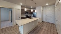 This contemporary single-floor residence is thoughtfully designed with a clean, modern aesthetic throughout. The open-concept kitchen serves as the heart of the home, showcasing a generous island with a white quartz countertop and undermount sink, dark espresso cabinetry, a classic subway tile backsplash, and a full suite of stainless steel appliances including a refrigerator, range, microwave, and dishwasher. Pendant lighting above the island adds a stylish finishing touch, while wood-look luxury vinyl plank flooring flows seamlessly throughout the main living areas.

The living area is bright and open, featuring a ceiling fan, neutral walls, and a large window that allows natural light to fill the space. The bedrooms are carpeted for comfort, each offering windows with blinds for natural light and privacy. The primary bedroom includes a ceiling fan and direct access to a well-designed en-suite bathroom.

The primary bathroom is particularly notable, featuring dual vanities with dark cabinetry and quartz countertops, a glass-enclosed walk-in shower with tile surround, wood-look flooring, and a spacious walk-in closet with built-in shelving. A secondary bathroom offers a single vanity with matching dark cabinetry, quartz countertop, and a tub-shower combination. The overall palette is neutral and cohesive, creating a clean, move-in-ready atmosphere throughout.