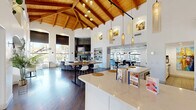 Located at 14435 South 48th Street in Phoenix, AZ, this single-floor community space makes an immediate impression with its dramatic vaulted ceilings adorned with exposed wood beams and warm tongue-and-groove paneling. The open-plan layout flows seamlessly across rich dark hardwood flooring, connecting multiple functional zones into one cohesive, inviting environment.

The kitchen is a standout feature, outfitted with white shaker cabinetry, a marble-style quartz countertop island with bar seating, stainless steel appliances including a professional range with hood, a French door refrigerator, and a marble tile backsplash. Elegant pendant lighting hangs above the island, and sliding glass doors provide direct access to an outdoor patio.

The main gathering area centers around high communal tables and modern bar-height chairs, with a stone-surround fireplace and wall-mounted television serving as a focal point. Arched windows and oversized roller shades frame views of the lush Phoenix landscape, flooding the space with natural light. A cozy lounge nook features a curved sectional sofa accented with colorful throw pillows, surrounded by tall windows and greenery.

A separate billiards area with a full-size pool table and a dedicated dining zone with arched window views round out the layout, making this a well-appointed, multi-use space designed for both community engagement and relaxed recreation.