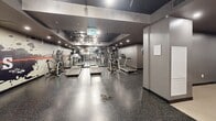 Located at 2475 Hurontario Street in Mississauga, Ontario, this fitness centre offers a well-appointed exercise space designed to support a full range of workout routines. The layout is thoughtfully organized into distinct zones, accommodating both cardio and strength training needs.

The cardio area is generously equipped with multiple treadmills and elliptical cross-trainers, positioned alongside a full-length mirrored wall that amplifies the sense of space and allows users to monitor their form. Durable speckled rubber flooring runs throughout this section, providing excellent grip and impact absorption.

The strength training area features a multi-function cable machine, a set of dumbbells on a tiered rack, an adjustable weight bench, and a stability ball, offering a comprehensive free weights zone. A wall-mounted punching pad adds an option for functional and martial arts-style training.

A bold, graphic feature wall with a dynamic fitness-themed mural serves as a striking visual focal point, adding energy to the environment. Track lighting and recessed ceiling fixtures provide bright, even illumination throughout the space. The dark ceiling and grey walls create a sleek, modern aesthetic that is both motivating and functional.

Overall, this fitness centre is a well-rounded facility suited for residents or building occupants seeking convenient, on-site access to professional-grade exercise equipment.