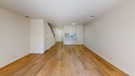 Located at 39900 Blacow Rd in Fremont, CA, this two-story, 2-bedroom, 2-bathroom home offers a practical and well-organized layout spread across two floors. The main level features a spacious open living area finished with warm wood-tone flooring that extends throughout the home. A sliding glass door dressed with vertical blinds fills the living space with natural light and provides access to an outdoor area. The kitchen is positioned adjacent to the living room, featuring a pass-through window and compact white cabinetry, keeping the lower level feel open and connected. A staircase with a classic railing leads to the upper floor, which houses both bedrooms and a hallway. The primary bedroom offers a comfortable footprint with wood flooring and a wide horizontal window fitted with blinds, framing views of surrounding greenery. The second bedroom mirrors the clean, neutral aesthetic with white walls and the same warm flooring. Two bathrooms serve the home, including one featuring a full tub-shower combination with white tile surround. Throughout the home, a consistent palette of white walls and light wood flooring creates a clean, cohesive look that provides a neutral canvas ready for personalization.