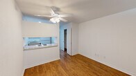 Located in Metairie, Louisiana, this single-floor studio offers a practical and well-organized layout that makes efficient use of its compact footprint. The main living area features warm wood-look flooring throughout, crisp white walls, and a ceiling fan with integrated lighting that keeps the space bright and comfortable. A pass-through kitchen counter with a granite-style surface connects the cooking area to the living space, offering built-in shelving and an electric cooktop — an efficient design that promotes an open feel. The kitchen is equipped with a refrigerator and sink, visible through the pass-through window. A hallway lined with multiple doors provides access to generous closet storage, including a wire-rack closet ideal for organization. The sleeping area is distinguished by soft carpeting underfoot, a wall-mounted HVAC unit, and a window fitted with blinds that allow natural light while maintaining privacy. Built-in open shelving adds a functional architectural detail that separates zones within the open layout. The overall aesthetic is clean and neutral, with white trim and consistent finishes throughout, creating a move-in ready space suited for those seeking a low-maintenance, efficiently designed home in Metairie.
