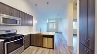This 550 square foot apartment in Huntington Beach offers a thoughtful blend of comfort and efficiency. The single-story layout comprises one bedroom, one bathroom, a modern kitchen, and additional functional spaces including a hallway and closet. The primary bedroom, measuring 120 square feet, provides a cozy retreat with a large window allowing natural light to flood the space.

The bathroom showcases a sleek design with a glass-enclosed shower, wood-finish vanity, and contemporary lighting. The kitchen is a highlight, featuring stainless steel appliances, including a refrigerator, stove, and built-in microwave. Dark wood cabinetry contrasts beautifully with light countertops and a subway tile backsplash.

Throughout the apartment, warm wood-look flooring creates a cohesive and inviting ambiance. The open-concept design maximizes the available space, with a breakfast bar separating the kitchen from the living area. Recessed lighting and pendant fixtures add to the modern aesthetic.

Large windows in the living area and bedroom not only brighten the space but also offer pleasant views of the surrounding greenery, enhancing the connection to the outdoors. This apartment combines functionality with style, making efficient use of its compact footprint while maintaining a sense of openness and light.