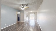 Located in the heart of Boerne, TX, this single-story, 2-bedroom, 1-bathroom home offers a well-designed layout with modern updates throughout. The open-concept living and dining area is anchored by rich, dark hardwood-style flooring, soft blue-gray accent walls, and a ceiling fan with light kit. A sliding glass door at the far end of the living space invites natural light and provides outdoor views framed by mature Texas oak trees.

The kitchen is a standout feature, showcasing granite countertops, a peninsula with a built-in sink and pendant lighting, crisp white shaker-style cabinetry, a tile backsplash, and black appliances including a range and refrigerator. A window above the counter brings in additional natural light.

Both bedrooms are carpeted for comfort, each equipped with a ceiling fan and closet access. The primary bedroom offers a generous footprint with ample room for furnishings. The second bedroom features a window with a view of the surrounding landscape.

The bathroom is clean and functional, featuring wood-style flooring, a white vanity, a tiled tub-shower combination, and open shelving for storage.

Outside, the grounds feature stone retaining walls, gravel landscaping, and mature oak trees, reflecting the natural Texas Hill Country setting.