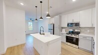 Located on Constitution Ave in Colorado Springs, CO, this well-appointed one-bedroom, one-bathroom residence offers a thoughtfully designed single-level layout. The open-concept kitchen and living area serves as the heart of the home, anchored by a striking white kitchen island with a built-in sink and matte black faucet, illuminated by a trio of pendant lights with brass accents. The kitchen features crisp white shaker cabinetry, a hexagonal tile backsplash, stainless steel appliances including a refrigerator, range, and microwave, and light wood-tone luxury vinyl plank flooring that flows throughout the entire space. A ceiling fan adds comfort to the living area, which benefits from natural light through a window overlooking greenery. The bedroom is a bright, serene retreat with multiple windows framing outdoor views, a ceiling fan, and continued wood-tone flooring. A private hallway connects the bedroom to the full bathroom, which is finished with gray cabinetry, a sleek LED-lit vanity mirror, matte black hardware, and tile accent walls. A dedicated closet and in-unit laundry area complete this efficiently designed residence, offering modern comfort and style throughout.
