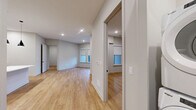 This thoughtfully designed 2-bedroom, 2-bathroom residence at 51 Okner Pkwy in Livingston, NJ offers a clean, modern aesthetic across a single floor. Light wood-tone flooring flows seamlessly throughout, complementing the neutral gray palette and recessed lighting found in every room.

The open-concept kitchen is a standout, showcasing floor-to-ceiling dark cabinetry with brushed gold hardware, crisp white quartz countertops, a vertical tile backsplash, and a full suite of stainless steel appliances including a gas range and French door refrigerator. A large central island with pendant lighting anchors the space, which opens directly to the living area with access to a private balcony.

Both bedrooms are well-proportioned with natural light from large windows fitted with roller shades. The primary bedroom includes a spacious walk-in closet with built-in shelving and hanging systems. Four closets total provide generous storage throughout.

The primary bathroom features marble-look tile flooring, a dual-sink dark vanity with white quartz countertops, a large wall mirror, and a glass-enclosed walk-in shower with a rain showerhead. The second bathroom offers the same refined finishes with a tiled tub-shower combination. Additional conveniences include in-unit laundry and a dedicated utility room.