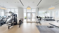 Located at 2010 Biscayne Blvd in Miami's vibrant Edgewater neighborhood, this generously sized fitness center offers a comprehensive, well-appointed workout facility across a single open floor. The space is bathed in natural light through floor-to-ceiling windows that frame sweeping views of the Miami skyline and Biscayne Bay, creating an energizing atmosphere throughout.

The cardio zone features a row of modern treadmills and a stair climber positioned directly in front of the expansive windows, allowing users to exercise while taking in the surrounding cityscape. A ceiling fan overhead ensures comfortable airflow in this bright, airy section.

The strength and free weights area includes a full dumbbell rack with a wide weight range, an adjustable workout bench, and floor-to-ceiling mirrored walls that amplify the sense of space. A dedicated functional training zone is equipped with a power rack, weight plates, medicine balls, battle ropes, resistance bands, a smart mirror, and a pull-up station, offering a diverse range of training modalities.

Multi-station cable and resistance machines are also available for targeted strength training. The facility features durable, easy-to-clean flooring with padded mat areas for stretching and floor exercises. A refreshment station with built-in cabinetry and a beverage cooler adds a convenient amenity. Double glass doors open to an outdoor terrace, extending the workout experience to the fresh Miami air.