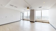 Located on the 44th floor of a prominent Dallas high-rise, this one-bedroom, three-bathroom residence offers an impressive urban living experience with panoramic skyline views visible from nearly every room. The open-concept living and kitchen area is bright and airy, featuring light hardwood flooring, a tray ceiling with a ceiling fan, and floor-to-ceiling windows that flood the space with natural light and frame dramatic vistas of the Dallas cityscape. The kitchen is well-appointed with warm wood cabinetry, stainless steel appliances including a French door refrigerator, a built-in microwave, and ample counter space, complemented by a wine cooler integrated into the kitchen island. The generously sized primary bedroom is carpeted for comfort, fitted with a ceiling fan, and wrapped in expansive floor-to-ceiling windows offering sweeping city views on multiple sides. The three bathrooms are clean and modern, with tile flooring and crisp white fixtures, one featuring a large window with a striking view of the Dallas skyline. A dedicated laundry room houses a full-size washer and dryer alongside shelving and storage. The overall ambiance of the residence is sleek, contemporary, and light-filled, with an emphasis on the remarkable elevated perspective of downtown Dallas.