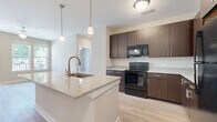 This single-floor residence at 3902 W Tyvola Rd in Charlotte, NC offers a thoughtfully designed layout with contemporary finishes throughout. The kitchen serves as a central highlight, showcasing rich dark-brown cabinetry, light granite countertops, and light wood-tone flooring. A central island with a built-in sink and pendant lighting above adds both functionality and style, while black appliances—including a range, microwave, and refrigerator—complete the space.

The living area features light wood-tone flooring, a ceiling fan, and large windows alongside a glass door that opens to a private balcony, allowing abundant natural light and outdoor views. The neutral warm-beige walls create a cohesive, inviting atmosphere throughout the common areas.

Bedrooms are finished with plush carpeting and neutral tones, with select rooms offering large windows that frame outdoor views. The bathrooms are well-appointed, featuring dark wood vanities, granite countertops, dual sinks, and light wood-tone flooring. One bathroom includes a separate water closet and walk-in shower, while another features a soaking tub and an adjacent walk-in closet with built-in shelving, providing practical storage solutions throughout the home.