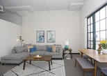 This single-floor loft-style residence blends industrial character with comfortable living. The open-concept living and dining area is the centerpiece of the space, highlighted by large, multi-pane grid windows that flood the room with natural light and offer sweeping urban views. Soaring ceilings with exposed elements add to the loft aesthetic, while plush carpeting grounds the space with warmth and comfort.

The kitchen is well-appointed with warm-toned wood cabinetry, granite-style countertops, a classic white subway tile backsplash, and wood-look vinyl plank flooring. Black appliances, including a dishwasher, complete the functional layout.

The space includes two bedrooms, both carpeted and designed for restful retreat. One bedroom features an exposed industrial ceiling with visible ductwork and a ceiling fan, along with a sliding wood-door closet. The other is a quieter, more intimate room with soft, neutral tones.

The full bathroom is finished with wood-look vinyl plank flooring, warm wood cabinetry, granite-style countertops, an undermount sink, and a shower-tub combo with a classic white curtain. A large mirror above the vanity enhances the sense of space. Overall, the residence offers a distinctive urban loft ambiance with practical, well-maintained finishes throughout.