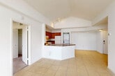 This 2-bedroom, 2-bathroom residence in Dania Beach, Florida offers a well-organized single-floor layout with notable architectural character. The open living area is defined by vaulted, tray ceilings that lend a sense of height and airiness, with light tile flooring running throughout the main living spaces.

The kitchen is centrally positioned and features warm wood cabinetry, dark granite-style countertops, white appliances including a range and refrigerator, and a peninsula with additional counter space that opens toward the living area. A stacked in-unit washer and dryer is conveniently tucked just off the kitchen behind louvered doors.

One bedroom benefits from sliding glass doors that open to a private balcony overlooking a pool area framed by lush palm trees, offering a distinctly Florida ambiance. This room features high vaulted ceilings and tile flooring. The primary bedroom is carpeted, with elevated ceilings, a ceiling fan, and a closet with louvered doors.

The two bathrooms each maintain a clean, functional design—one featuring a tub-shower combo and the other a walk-in shower—both finished in white tile. The overall aesthetic is bright and neutral throughout.