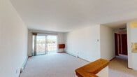 This single-floor unit offers a clean, functional layout designed for comfortable everyday living. The spacious living room is bathed in natural light, courtesy of large sliding glass doors that open onto a private balcony with open outdoor views — an ideal space for relaxing or enjoying the surrounding scenery. Baseboard heating runs throughout, ensuring year-round comfort. The galley-style kitchen is efficiently organized, featuring white cabinetry, light granite-look countertops, a double sink, and white appliances including a refrigerator, electric range, and built-in microwave — all set on easy-care tile flooring. Two well-proportioned bedrooms are finished with plush carpeting, warm wood trim, and windows that invite natural light and outdoor views. The bedrooms offer a calm, neutral palette with ample wall space. The full bathroom is thoughtfully equipped with a tiled tub-and-shower combination, safety grab bars for accessibility, a vanity with sink, and a wall-mounted mirror. Throughout the unit, consistent warm wood door and baseboard trim provides a cohesive finishing touch, while the neutral white walls and light carpeting create a bright, versatile backdrop ready for personalization.