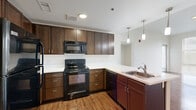 Located in Denver, CO 80220, this 2-bedroom, 2-bathroom residence offers a thoughtfully designed single-floor layout. The open-concept kitchen is a standout feature, equipped with rich dark wood cabinetry, black appliances including a refrigerator, electric range, and built-in microwave, complemented by a peninsula with a stainless steel sink and stylish pendant lighting overhead. Hardwood-style flooring flows throughout the kitchen and main living areas, creating a warm, cohesive aesthetic. The living room is bright and airy, benefiting from natural light through large windows fitted with blinds. Both bedrooms are carpeted and generously proportioned, with the primary bedroom offering direct access to a walk-in closet and ample natural light from tall windows. Each bedroom is served by its own bathroom, both featuring a tub-shower combination, a dark wood vanity with white countertops, and hardwood-style flooring. A second closet provides additional storage. The hallway connects all rooms efficiently, contributing to the unit's practical flow. The clean, neutral color palette throughout enhances the sense of openness and light, making this a well-appointed and functional residence.