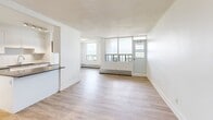 Located at 15 Eva Rd in Toronto's Etobicoke neighbourhood, this well-appointed 3-bedroom, 1-bathroom unit offers a thoughtfully designed single-floor layout with a clean, contemporary aesthetic throughout. Light wood laminate flooring runs seamlessly across all rooms, complemented by crisp white walls and bright, airy finishes that create a welcoming atmosphere.

The open-concept kitchen and living room area serves as the heart of the unit. The galley-style kitchen is outfitted with white shaker cabinetry, a grey quartz countertop, a subway tile backsplash, stainless steel appliances including a refrigerator and dishwasher, and a double undermount sink. Track lighting illuminates the workspace efficiently. The adjacent living room is generously sized, featuring a wall of large windows that flood the space with natural light and offer expansive views of the Toronto skyline.

The primary bedroom is a comfortable retreat with a large window showcasing city views. Two additional bedrooms provide flexible space for various needs, connected via well-proportioned hallways with modern panel doors and chrome hardware. The full bathroom features classic white subway tile surrounding a full soaker tub with shower, paired with light wood-tone flooring for a clean, timeless finish. This unit combines functional design with modern touches in a prime Toronto location.