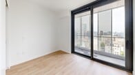 Located at 707 Terry Ave in Seattle, WA, this modern two-bedroom, two-bathroom residence offers a clean, contemporary design throughout its efficiently arranged single-floor layout. Light wood-tone flooring flows consistently across all rooms, complementing the crisp white walls and creating a bright, cohesive aesthetic.

A connecting hallway, illuminated by recessed lighting, links the living areas and provides a polished sense of flow through the space. The primary bedroom features sliding glass doors that open to sweeping views of the Seattle skyline, while a built-in sliding closet and direct access to an en-suite bathroom add everyday convenience. The second bedroom also benefits from natural light via a large window and includes a sliding closet for ample storage.

Both bathrooms are finished in a clean, minimalist style. One features full white subway tile surrounding a soaking tub and shower combination, paired with terrazzo-style flooring. The other bathroom mirrors this refined aesthetic with a floating vanity, frameless mirror, and a combination tub and shower. The kitchen, visible from the hallway, is outfitted with stainless steel appliances including a built-in oven and microwave. Throughout the residence, the design emphasizes simplicity, functionality, and a connection to the dynamic urban surroundings of downtown Seattle.