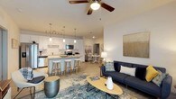 Parkside At The Beach presents a thoughtfully designed single-floor residence that blends modern finishes with a relaxed coastal aesthetic. The open-concept living and dining area is anchored by a comfortable living space with light wood-style flooring, a ceiling fan, and seamless flow into the kitchen and dining area. The kitchen is a standout feature, equipped with crisp white cabinetry, stainless steel appliances, a classic white subway tile backsplash, and a generously sized center island with pendant lighting and bar seating — ideal for casual dining or entertaining. The primary bedroom offers a serene retreat with carpeted flooring, a ceiling fan, and coastal-inspired décor. It connects to a well-organized walk-in closet with full-length hanging rods and shelving. The en-suite bathroom includes a wide vanity with white cabinetry, a large mirror, and built-in open shelving for added storage. Additional bedrooms are carpeted, naturally lit, and feature ample closet space, including walk-in options. Throughout the residence, a neutral color palette and clean lines create a bright, airy ambiance. The cohesive design and quality finishes make this space a comfortable and functional home near the beach.