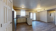 Located at 852 N 100 E in Tooele, Utah, this single-floor unit offers a well-designed, open-concept layout that connects the kitchen and living areas seamlessly. The kitchen is a standout feature, equipped with stainless steel appliances—including a refrigerator, range, microwave, and dishwasher—complemented by granite-style countertops and crisp white cabinetry. A peninsula provides additional prep space and casual seating. Natural light filters in through a window above the sink and a sliding glass door fitted with vertical blinds, which also provides exterior access. The living area extends generously from the kitchen, finished with durable wood-look plank flooring and accented by a chandelier overhead. A textured ceiling adds architectural character throughout the main living spaces. The bedrooms are carpeted for comfort, with windows offering natural light and neutral walls providing a clean backdrop. Two bathrooms mirror the home's consistent design aesthetic, each featuring white cabinetry, granite-style countertops, tub-shower combinations, and wood-look flooring. The overall interior palette of warm neutrals and modern finishes creates a cohesive, move-in-ready environment.