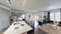 This single-floor residence showcases a thoughtfully designed open-concept layout that seamlessly connects the kitchen, dining, and living areas, creating a cohesive and functional living environment. Throughout the space, wood-style flooring, neutral gray crown molding, and crisp white walls establish a contemporary aesthetic.

The kitchen is a standout feature, equipped with gray shaker-style cabinetry, stainless steel appliances, a subway tile backsplash, and a generous island with a white quartz countertop and seating for multiple guests. Pendant lighting and a track lighting system illuminate the space effectively.

The dining area flows naturally from the kitchen and is brightened by a sliding glass door that opens to a private balcony, offering outdoor views. The living room receives ample natural light through large windows and provides a comfortable, versatile setting.

The bedroom is a well-sized retreat featuring dark hardwood-style floors, direct balcony access, multiple windows, and an ensuite bathroom. The bathroom includes a dual-sink vanity with a white countertop, gray cabinetry, a soaking tub, and wood-style flooring, delivering a clean and functional finish throughout.